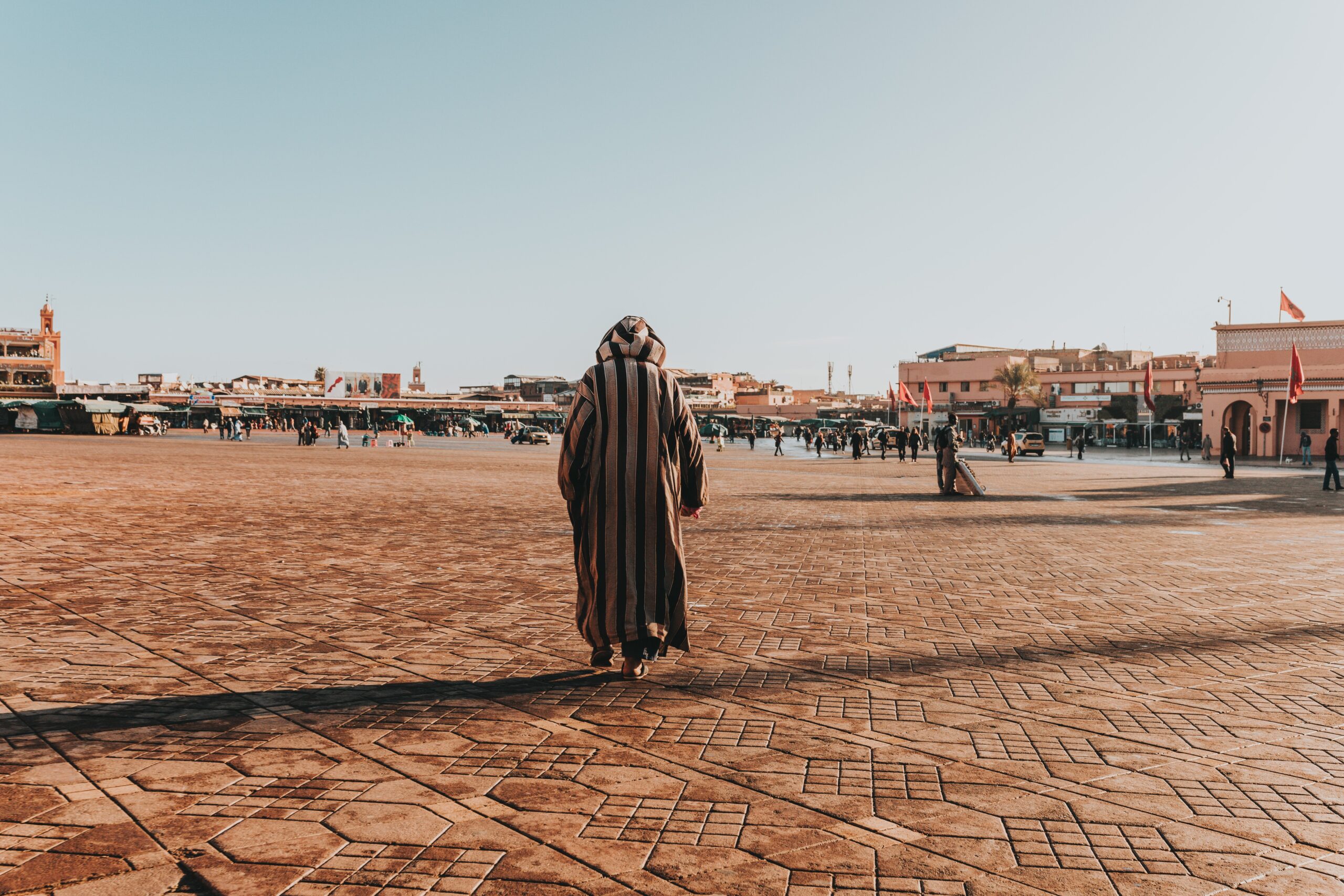 A sunny scenery of an Arabian male in stripped thawb walking in the big urban area